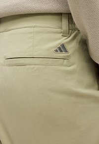 Μπεζ παντελόνι με πίσω τσέπη welt και μικρό μαύρο και μπεζ τρίγωνο λογότυπο στο πάνω δεξί μέρος.