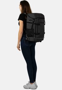 Schwarzer Stoff-Rucksack mit mehreren Fächern, verstellbaren Trägern und einem ausziehbaren Griff. Verfügt über eine seitliche Netztasche und Rollen.