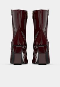 Bottines en cuir verni bordeaux avec talons carrés et fermetures éclair sur les côtés. La surface a une texture brillante et une construction sans couture.