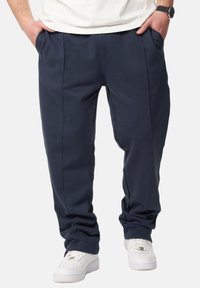 Marineblaue Jogginghosen mit lockerer Passform, seitlichen Taschen, glatter Textur und dezenten vorderen Nähten für zusätzliche Designakzente.