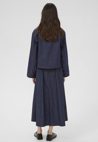 Denimowy komplet składający się z dopasowanej kurtki i długiej, zwiewnej spódnicy w głębokim indygo. Szyte akcenty widoczne wzdłuż szwów.