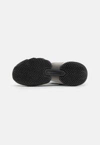 Semelle de chaussure de sport en caoutchouc noir, avec un motif de bande de roulement en zigzag et une section centrale lisse. Dessus gris clair avec des accents subtils.