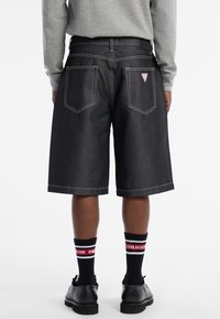 Shorts en denim foncé avec une coupe droite, des détails de couture supplémentaires, deux poches à l'arrière, et des chaussettes noires texturées avec des accents rouges et blancs.