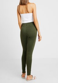 Gröna rutig leggings med hög midja, gjorda av ett stretchigt material. Bärs med en vit tanktop och sandaler, visas bakifrån.