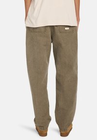 Braune, lässige Hose aus strukturiertem Baumwollstoff. Verfügt über zwei Gesäßtaschen und ein kleines Etikett am Bund. Wird mit einem hellen Hemd kombiniert.
