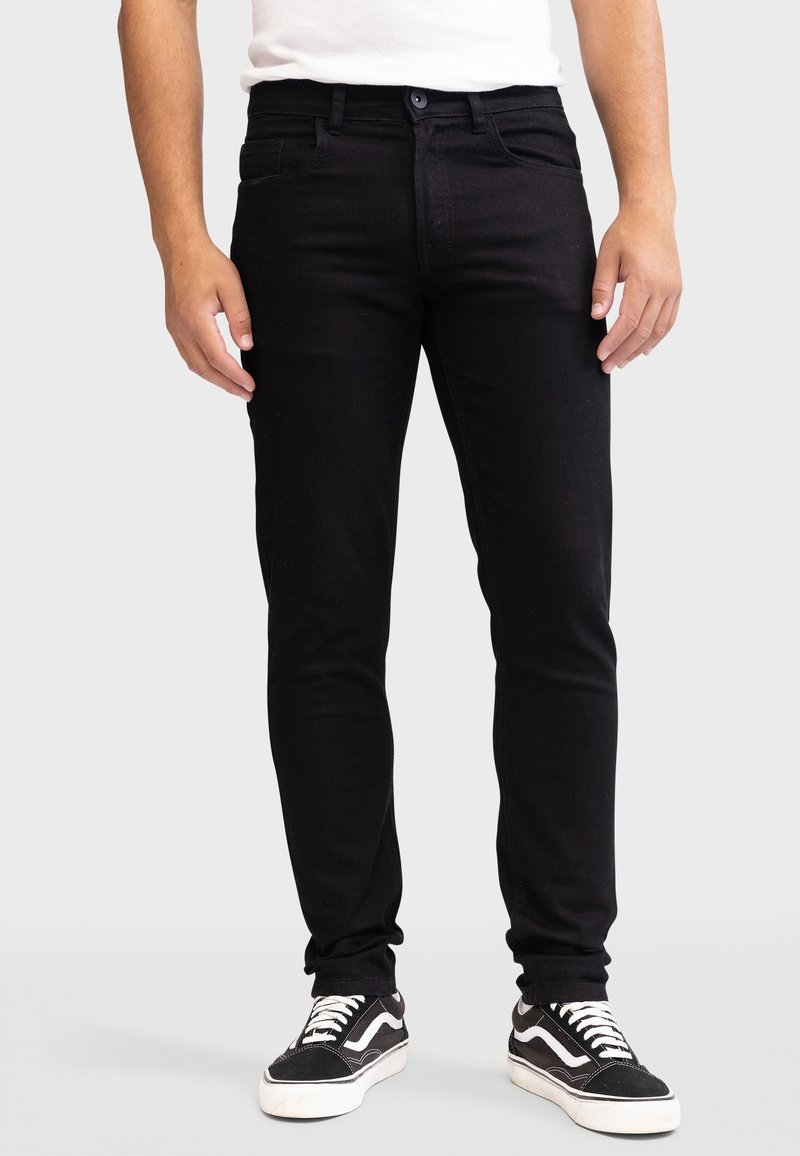 Jeans de mezclilla negra con un ajuste slim, que cuentan con bolsillos delanteros y trabillas para el cinturón. Combinados con zapatillas negras y blancas.