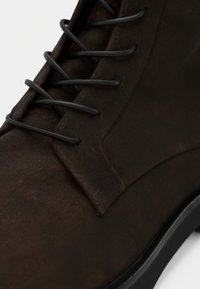 Bottine en cuir marron avec une finition mate, dotée de lacets noirs et d'un onglet distinct pour un enfilage facile. Semelle robuste avec profil bas.