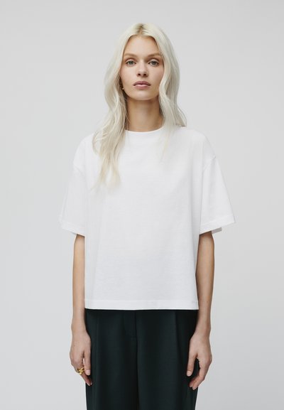 Camiseta de algodón blanca de corte relajado, con mangas cortas y escote redondo. Diseño minimalista con hombros sin costuras y dobladillo recto.
