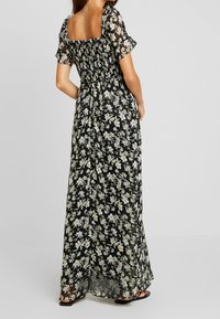 Maxiklänning i genomskinlig svart tyg med vita blommönster, smockad bodice, korta volangärmar och en öppen fyrkantig rygdesign.