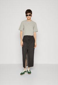 Grå t-skjorte med kort erme med tekst, svart denim maxi-skjørt med frontslipp, og grønne sneakers med hvite og beige detaljer.