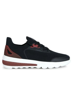 Zapatilla deportiva negra con parte superior de malla, acentos rojos y suela blanca con sección texturizada. Diseño de cordones con cuello acolchado.