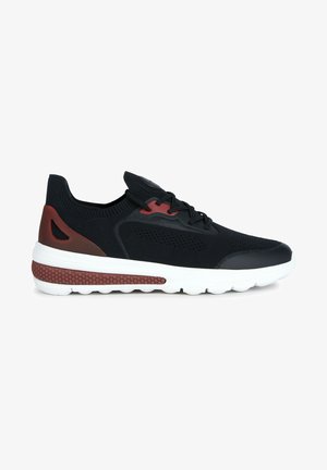 Zapatilla deportiva negra con parte superior de malla, acentos rojos y suela blanca con sección texturizada. Diseño de cordones con cuello acolchado.