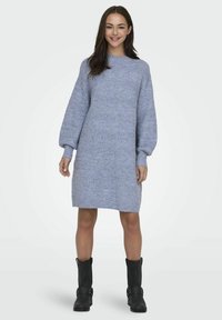 Blå strikket kjole med høy hals, lange pufferm og et teksturert mønster. Bæres med svarte ankelstøvler. Midt på låret lengde.