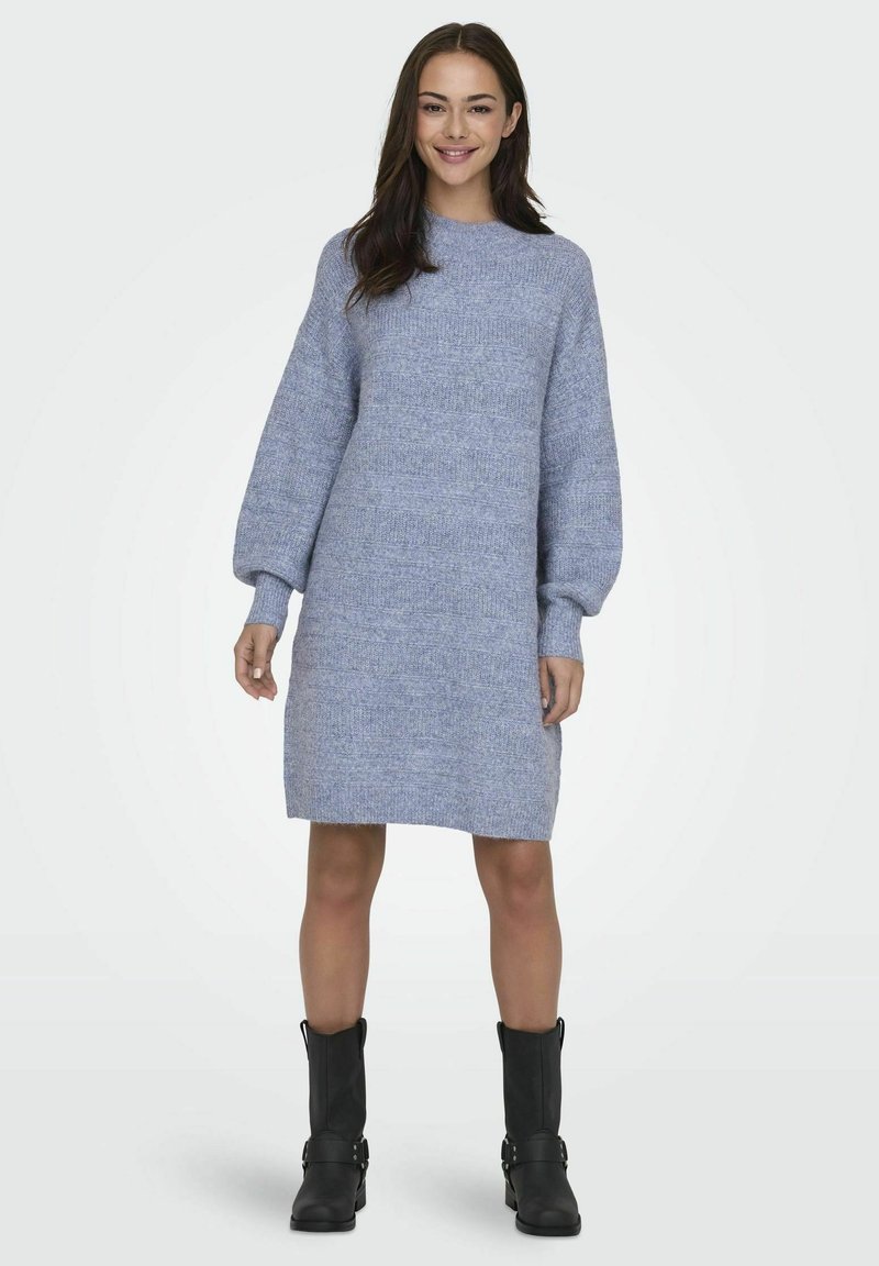 Blå strikket kjole med høy hals, lange pufferm og et teksturert mønster. Bæres med svarte ankelstøvler. Midt på låret lengde.