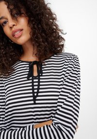 Czarny i biały top w paski z długimi rękawami, okrągłym dekoltem i detalem w postaci wiązania przy szyi. Gładka tekstura, casualowy fason.