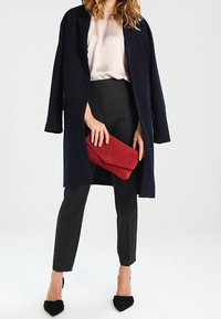 Marinefrakke, lyserød bluse, sorte skræddersyede bukser og sorte spidse hæle. Holder en rød clutch. Glat stof og struktureret design.