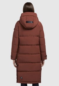 Lange, gevoerde bruine parka met capuchon, voorzien van een logopatch, knoopsluitingen bij de mouwen en zijsplitten voor extra bewegingsvrijheid. Geweven, gewatteerd ontwerp.