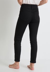 Jeans ajustados de mezclilla negra con una cintura alta, dobladillos enrollados y dos bolsillos traseros. La tela parece suave, con detalles de costura mínimos.