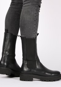 Schwarze Stiefeletten aus Leder und Elastik mit einer klobigen Sohle, strukturiertem Finish und Zugschlaufen an den Seiten.