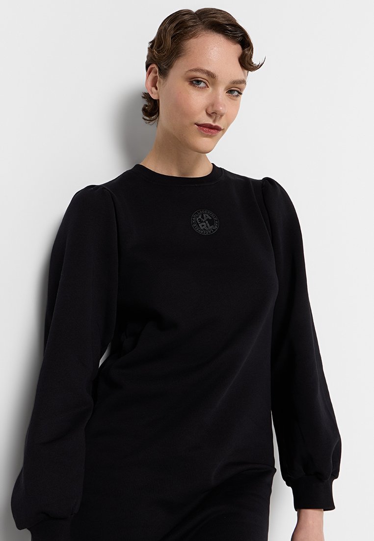 Sweatshirt noir avec des manches ballon et un col rond. Tissu texturé avec un petit logo en relief sur la poitrine.