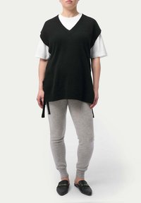 Svart stickad väst med V-ringning, bärs över en vit T-shirt. Matchas med grå byxor och svarta slip-on skor.