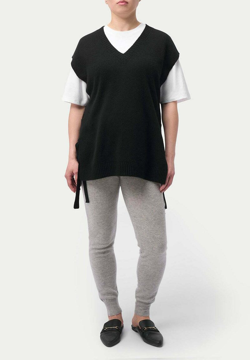 Svart stickad väst med V-ringning, bärs över en vit T-shirt. Matchas med grå byxor och svarta slip-on skor.