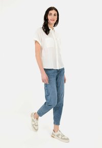 Weißes kurzärmeliges Button-up-Hemd mit zwei Fronttaschen, kombiniert mit hellblauen, taillierten Jeans und beigen Sneakers mit grauen Akzenten.