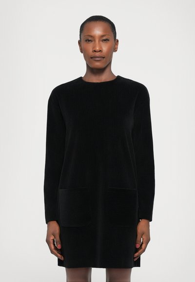 Robe en corduroy noir avec des manches longues, un col rond et deux poches avant. Texture douce, design à mi-cuisse et silhouette droite.