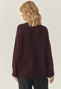 Burgundské pletené sveter so voľným strihom, rebrovanými manžetami a lemom, a okrúhlym výstrihom, doplnený prúžkovanými nohavicami. Mäkká textura.