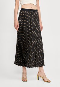 Geplooide zwarte rok met een metalen gouden paisleypatroon, met een zwarte elastische tailleband. Gecombineerd met gouden sandaaltjes met bandjes.