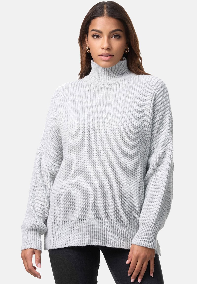Maglione lavorato a maglia grigio chiaro con colletto alto, vestibilità ampia, texture a coste e spalle cadenti, abbinato a jeans scuri.