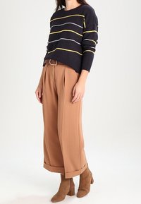 Marinrandig tröja med gula och grå linjer, parat med bruna plisserade vida byxor. Bruna klackstövlar vid vristen fulländar looken.