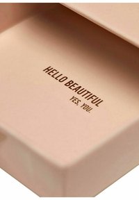 Ljusrosa rektangulär box inuti med präglad brun text som säger "HEJ VACKRA JA, DU." Slät struktur, minimalistisk design.