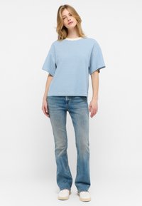 Camiseta de manga corta a rayas azul y blanca con un corte amplio, combinada con jeans acampanados de un azul claro y zapatillas blancas.