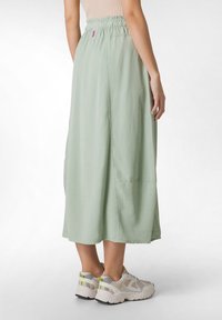 Gonna midi verde chiaro con cintura elastica, caratterizzata da una vestibilità comoda e una sottile texture. Indossata con sneakers neutre e un top aderente.
