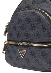 Mochila negra con textura y herrajes dorados, que presenta un destacado logotipo triangular y tela con patrón. Cierres de doble cremallera y diseño elegante.