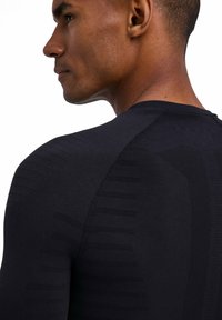 Czarna sportowa koszulka o dopasowanym kroju z teksturowanymi paskami na ramionach i plecach, podkreślająca bezszwową konstrukcję ubrania.