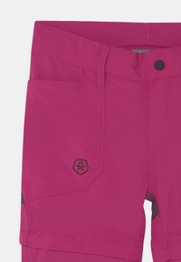 Pantalones ligeros de color rosa con una textura suave, que presentan costuras negras y un logo en el bolsillo delantero. Incluye un cierre estándar en la cintura.