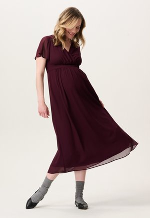 Bordeaux midi-jurk met korte, zorgeloze mouwen, een v-hals en een verzamelde taille. Lichtgewicht stof, vloeiende silhouet, gecombineerd met grijze sokken en zwarte schoenen.