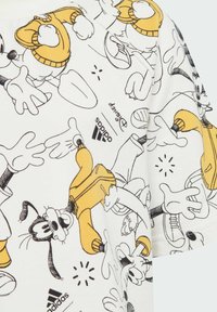 T-shirt bianca con contorni neri di personaggi dei cartoni animati e accenti gialli. Il materiale sembra morbido con un design casual e maniche corte.