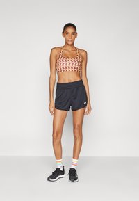 Sport bra with a brown geometric pattern, paired with black shorts. Features a fitted design, elastic waistband, and logo detail.