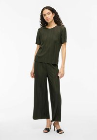 Completo a due pezzi color khaki con gonna plissettata, caratterizzato da un top ampio a maniche corte e pantaloni a gamba larga, realizzati in un materiale leggero e testurizzato.