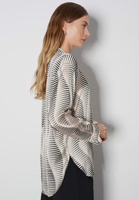 Long-sleeved blouse in cream with black vertical stripes, made from a lightweight, smooth fabric, featuring a curved hem and button cuffs.