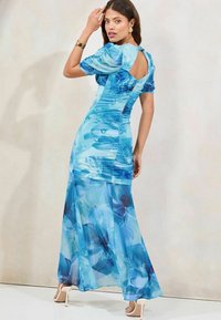 Rochie maxi floral albastră cu mâneci bufante și decupaj la spate. Prezintă o fustă fluidă și un overlay transparent cu modele mari de flori.