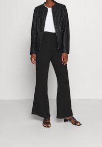 Veste en cuir noir avec un col rond, associée à un pantalon noir à jambes larges et des sandales à lanières noires. T-shirt blanc en dessous.