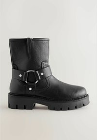 Black leather ankle boot with a textured finish, wide strap featuring a circular silver buckle, and a thick, rugged sole.