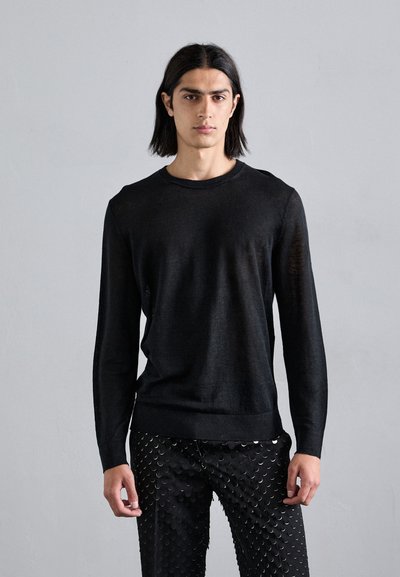 Schwarzer, langärmeliger Strickpullover mit Rundhalsausschnitt und gerippten Bündchen, kombiniert mit schwarzen, strukturierten Hosen mit runden Akzenten.