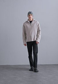 Heled hall, veerandsi tõmbega fliispullover, mis on kantud musta särgi kohal, tumedate pükste ja mustade saapadega. Lisandiks triibuline beanie.