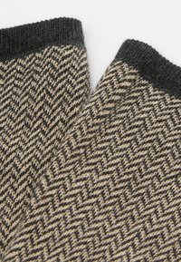 Gewebte schwarze und beige Socken mit einem Fischgrätmuster, versehen mit einem einfarbigen schwarzen Bündchen. Strukturierter Stoff mit einem weichen, warmen Aussehen.