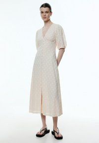 Helles rosa Kleid mit weißen Punkten, V-Ausschnitt, Puffärmeln und einer Knopfleiste. Kombiniert mit schwarzen Plateausandalen.